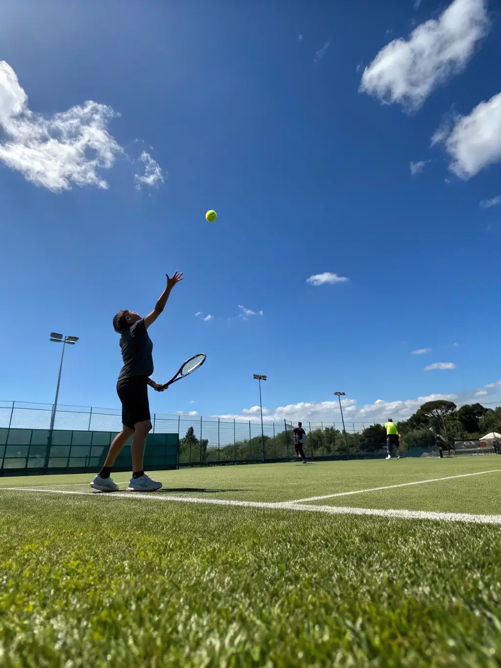 Image of a specialized tennis clinic focusing on serve technique, with a coach demonstrating proper form and players practicing.